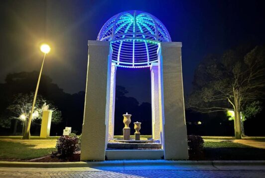 Attached image file 'n Koepelvormige paviljoen met blou ligte gloei snags en beklemtoon drie vase binne. Straatligte en bome omring die struktuur, en die toneel is stil en vreedsaam.