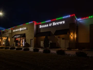 'n Koffiewinkel genaamd Beans & Brews en 'n bruidswinkel is langs mekaar in 'n plein in die nag, met kleurvolle vakansieligte wat die dak omlyn en 'n brandende straatlamp daar naby.