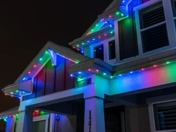 'n Huis in die nag word versier met rooi, groen en blou LED-ligte langs die dakrande en dakrand, wat 'n feestelike atmosfeer skep.