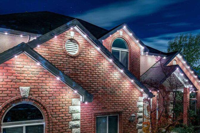 Attached image file 'n Baksteenhuis in die nag met wit LED-ligte wat die dak en gewels omlyn, wat die argitektoniese kenmerke onder 'n gedeeltelik bewolkte sterrehemel beklemtoon.