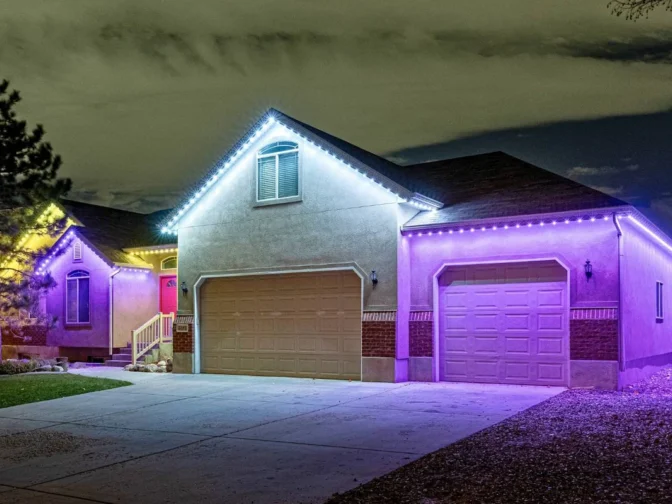'n Huis in die nag met wit en pers LED-ligte wat die dak en motorhuis omlyn. Die oprit en erf is sigbaar, en die omliggende area is dof verlig.